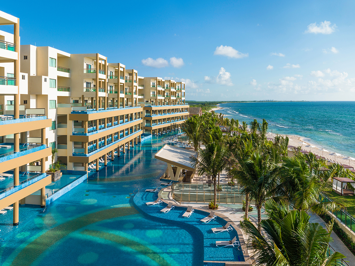 Large blue tropical resort pool with palm trees next to beach and ocean