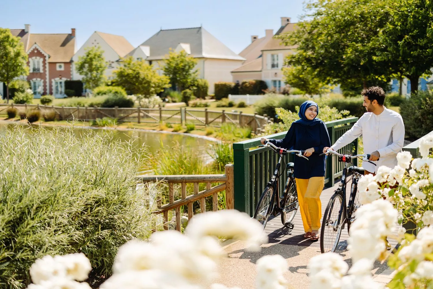 Couple walking with bicycles over the bridge next to a beautiful lake